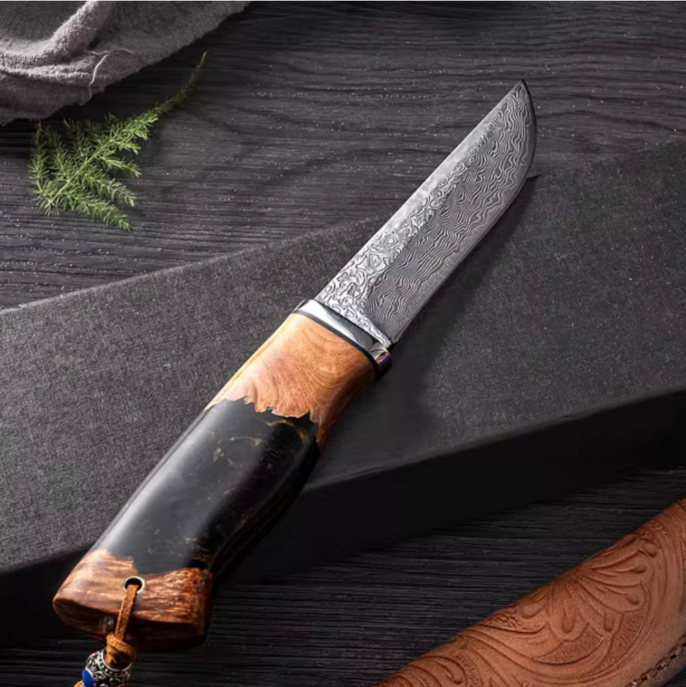 A Predator Japanese Damascus Steel Knife with a unique wave pattern blade, featuring an ergonomic handle with stabilized wood and resin, placed on a dark surface with a leather sheath partially visible.